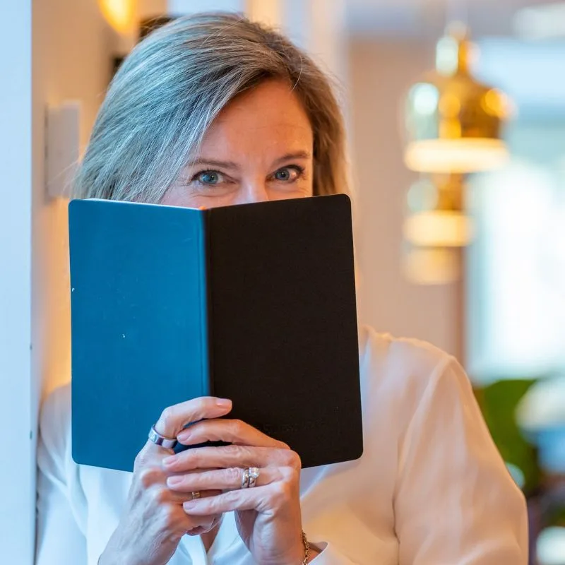 Photo de Sacheen Sierro masquant une partie de son visage avec un livre pour inciter à découvrir sa page à propos